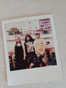 Auf dem Foto stehen drei Personen in Sommerkleidung. 